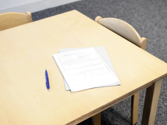 A white exam paper and black pen on a beige desk.