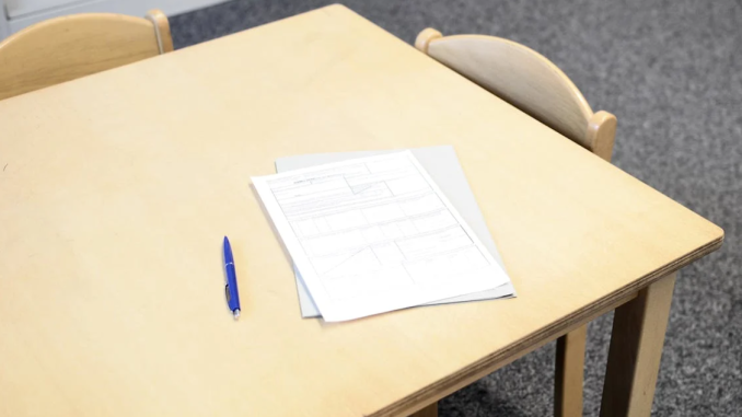 A white exam paper and black pen on a beige desk.