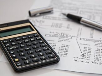 A black calculator on a white desk on top of some papers with maths calculations.