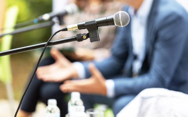 Microphone in focus against blurred people at round table event or business conference.